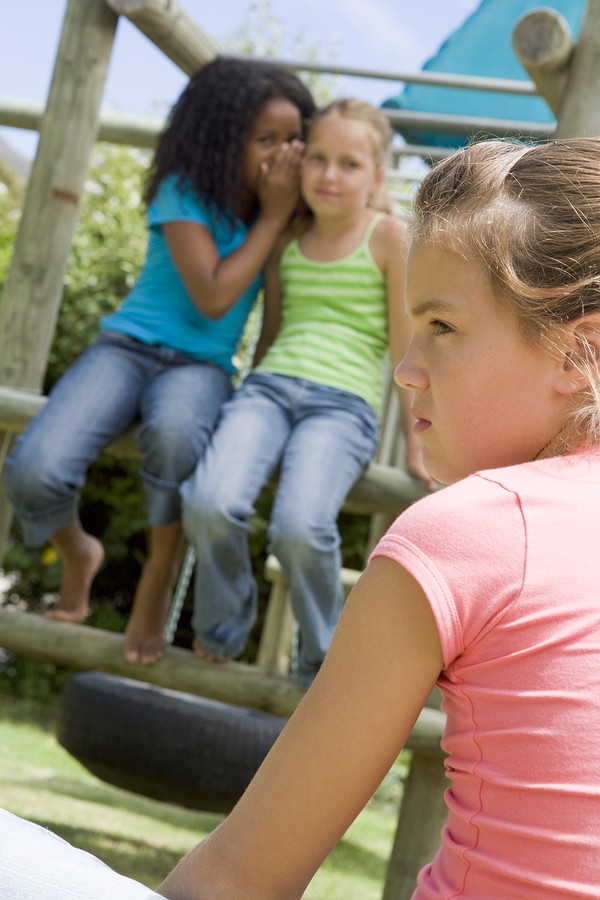 Two young girl friends at a playground whispering about other gi